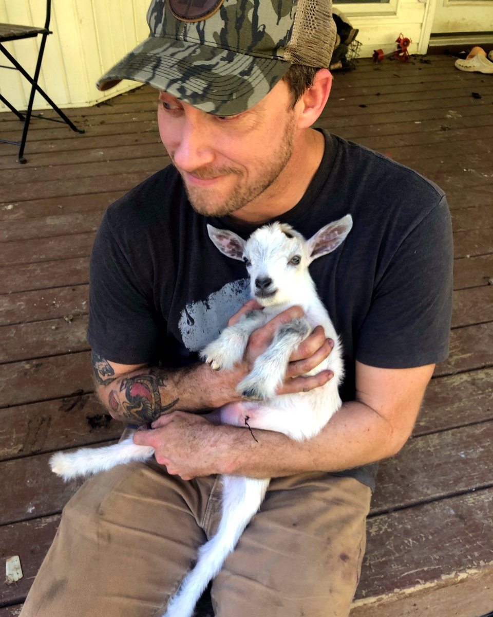 Kyle holding a baby goat on the porch of a Tennessee homestead