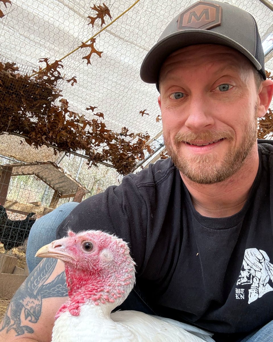Kyle holding a young white turkey in the chicken run on a Tennessee homestead
